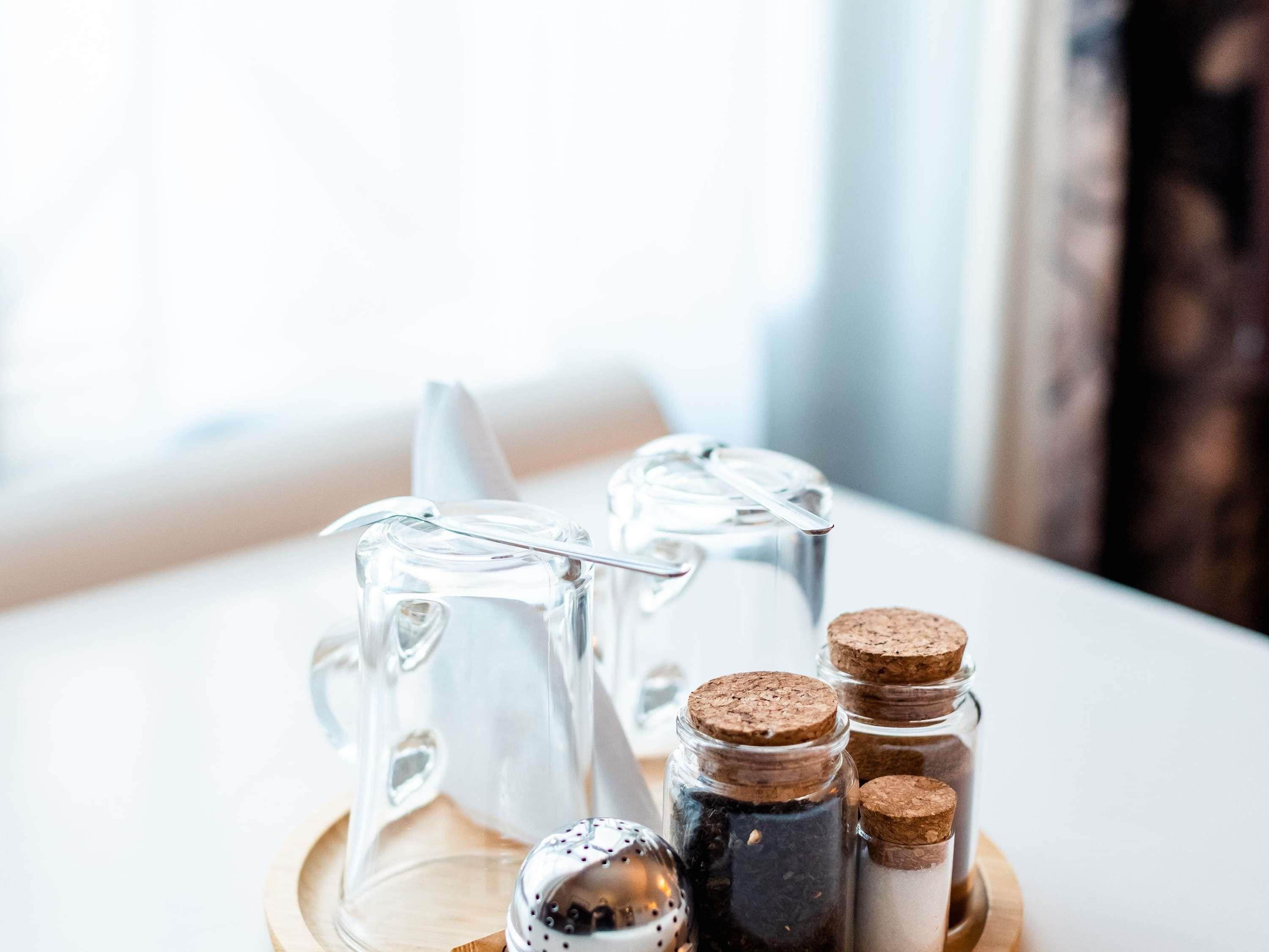 A clear glass pitcher and three small glass containers with cork stoppers on a wooden coaster.