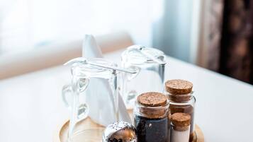 A clear glass pitcher and three small glass containers with cork stoppers on a wooden coaster.