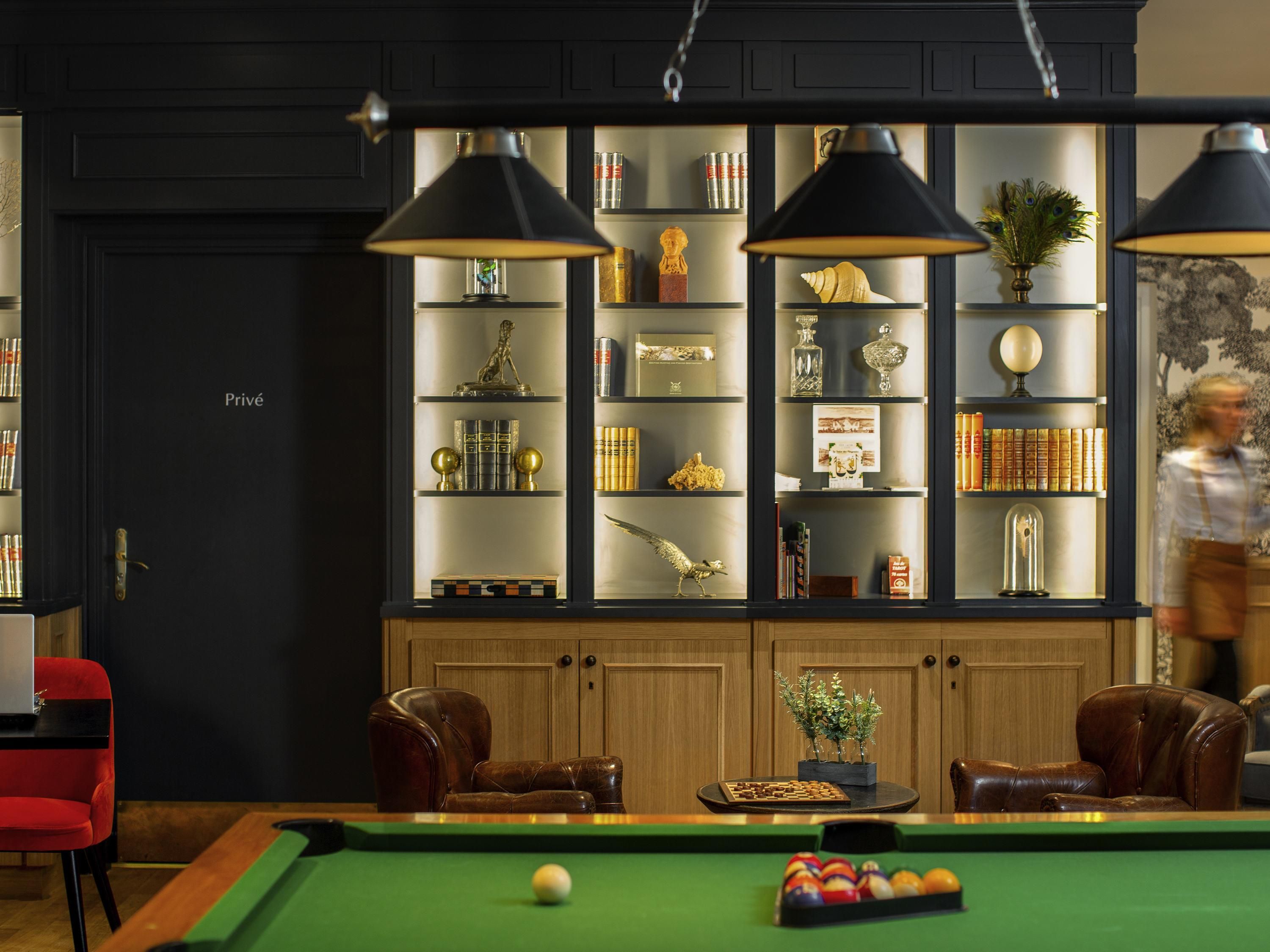 A billiards table with balls, a red chair, and a bookshelf with various items.
