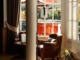 A room with a leather armchair, a table with a menu, and a window with a view of a wooden fence and greenery.