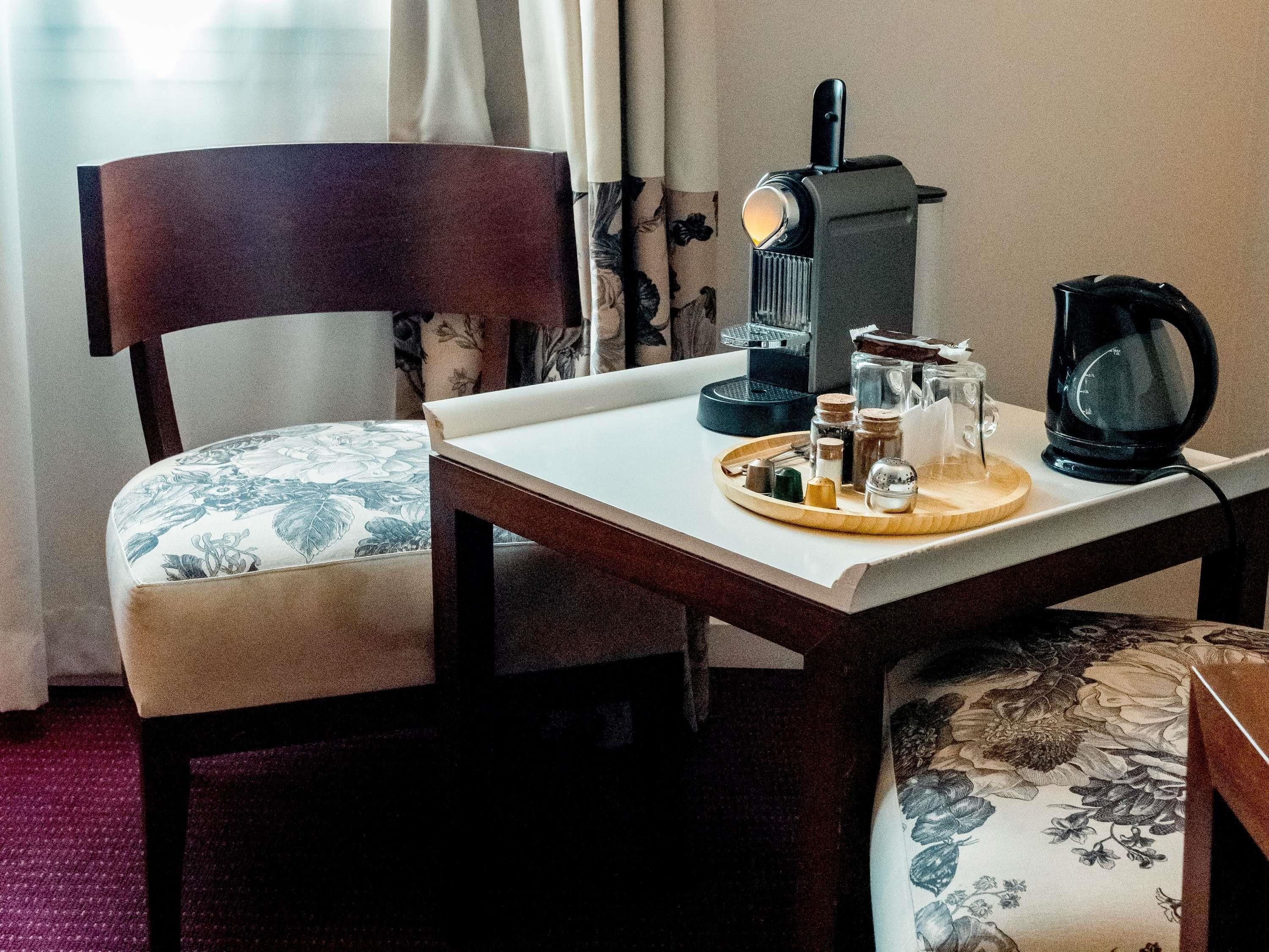 A dining area with a wooden table, a chair with floral upholstery, a coffee maker, and a tray with condiments.