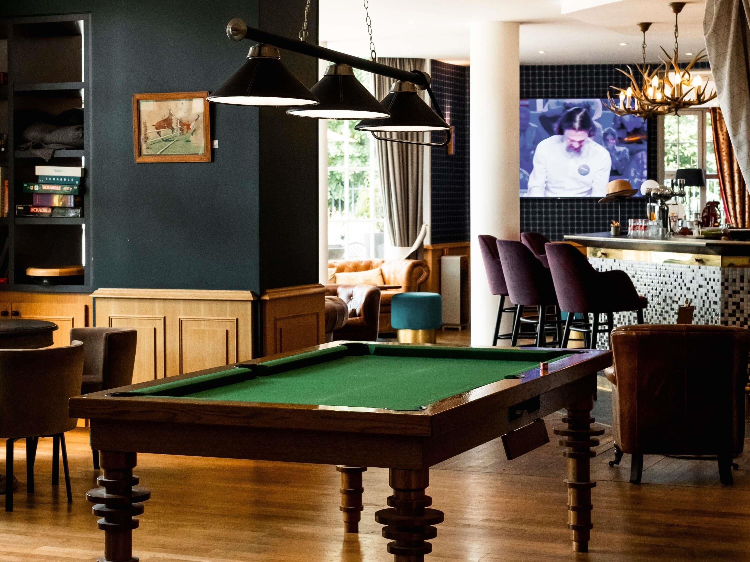 A billiards table in a room with a bar area, seating, and a television screen.