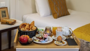 Bandeja de desayuno con cruasanes, frutas y una taza de café sobre una mesa de madera en una habitación de hotel.