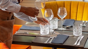 Una persona preparando una mesa con vasos transparentes y una copa de vino.