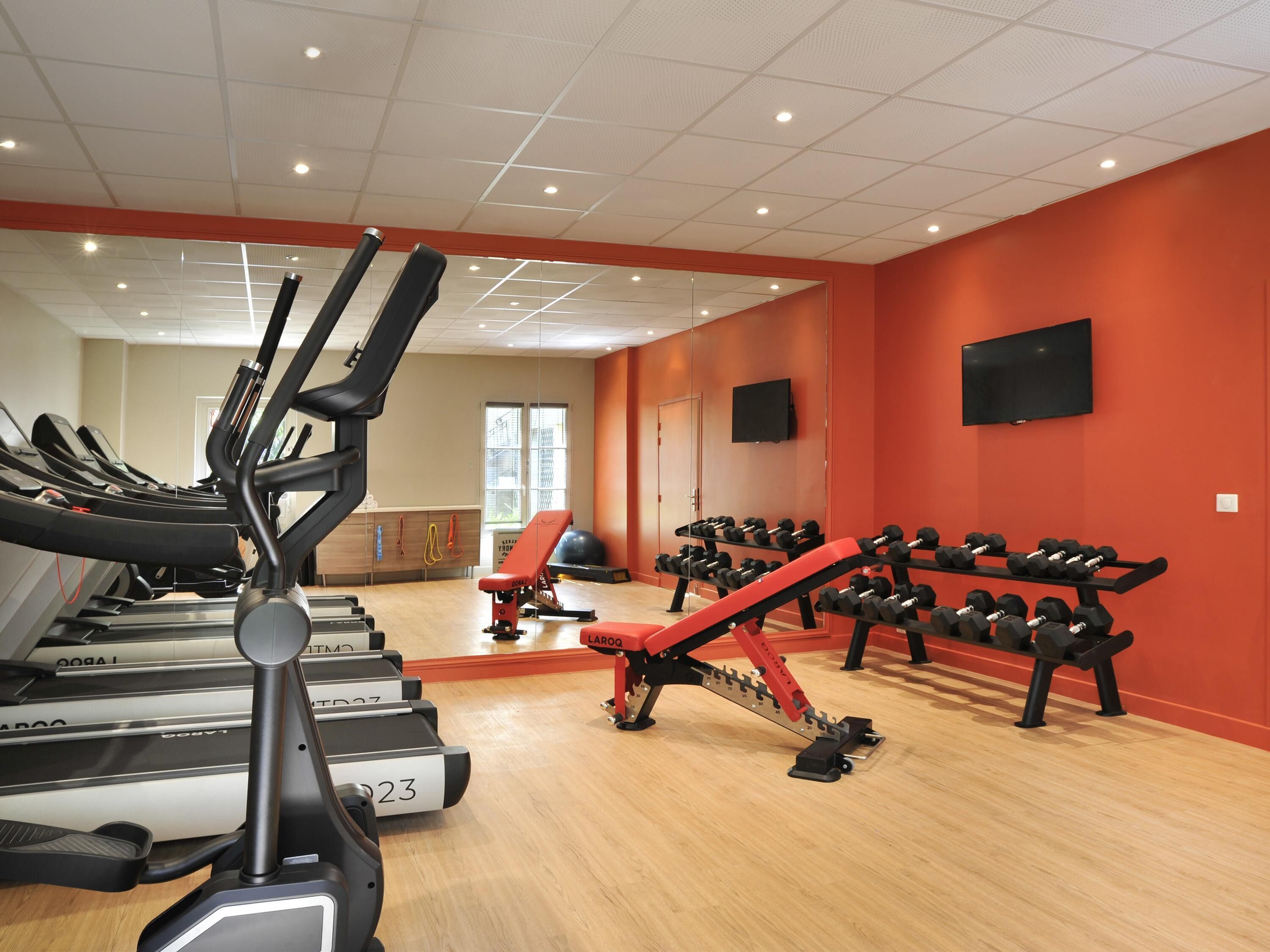 Een sportschool met loopbanden, een rode bank en een dumbbellrek.