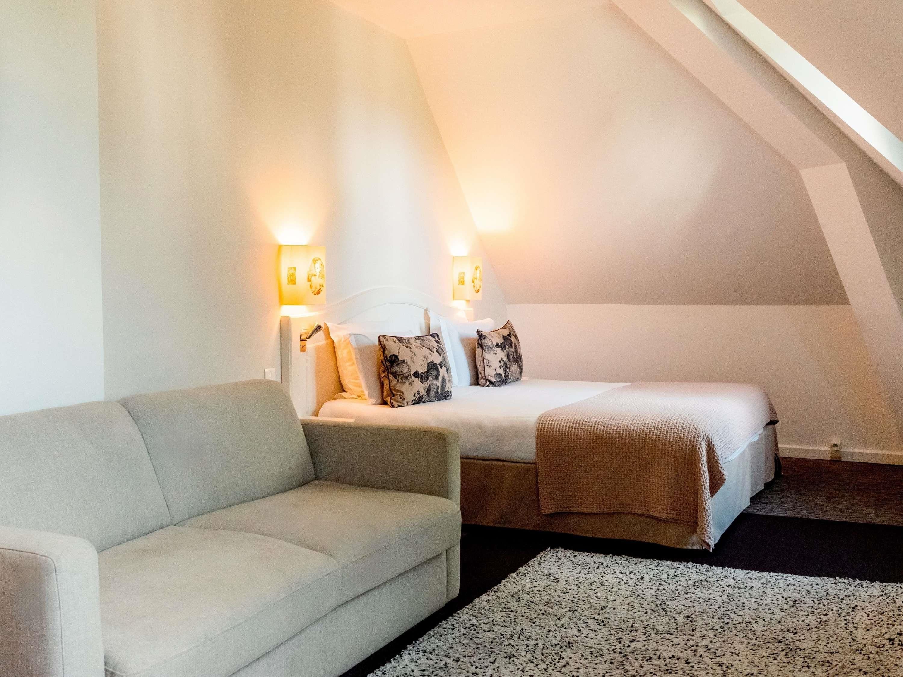 Un dormitorio con una cama, un sofá y dos lámparas de pared.