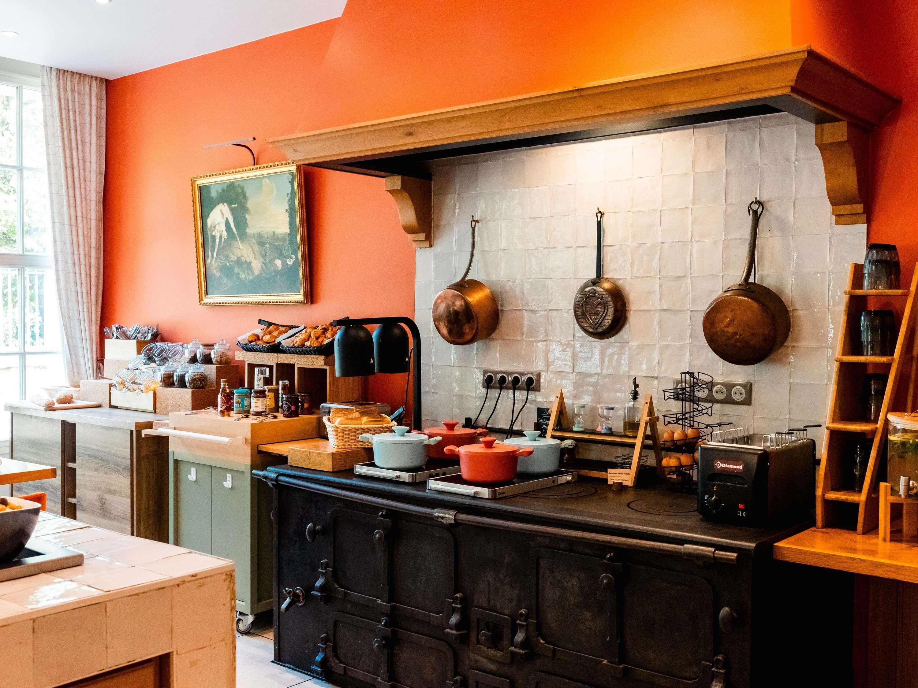 Une cuisine avec un four ancien, un porte-casseroles suspendu et un tableau accroché au mur.