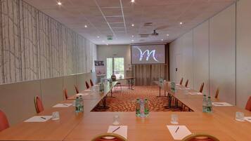 A conference room with a long table, chairs, water bottles, and a screen displaying the word 'Mercure'.