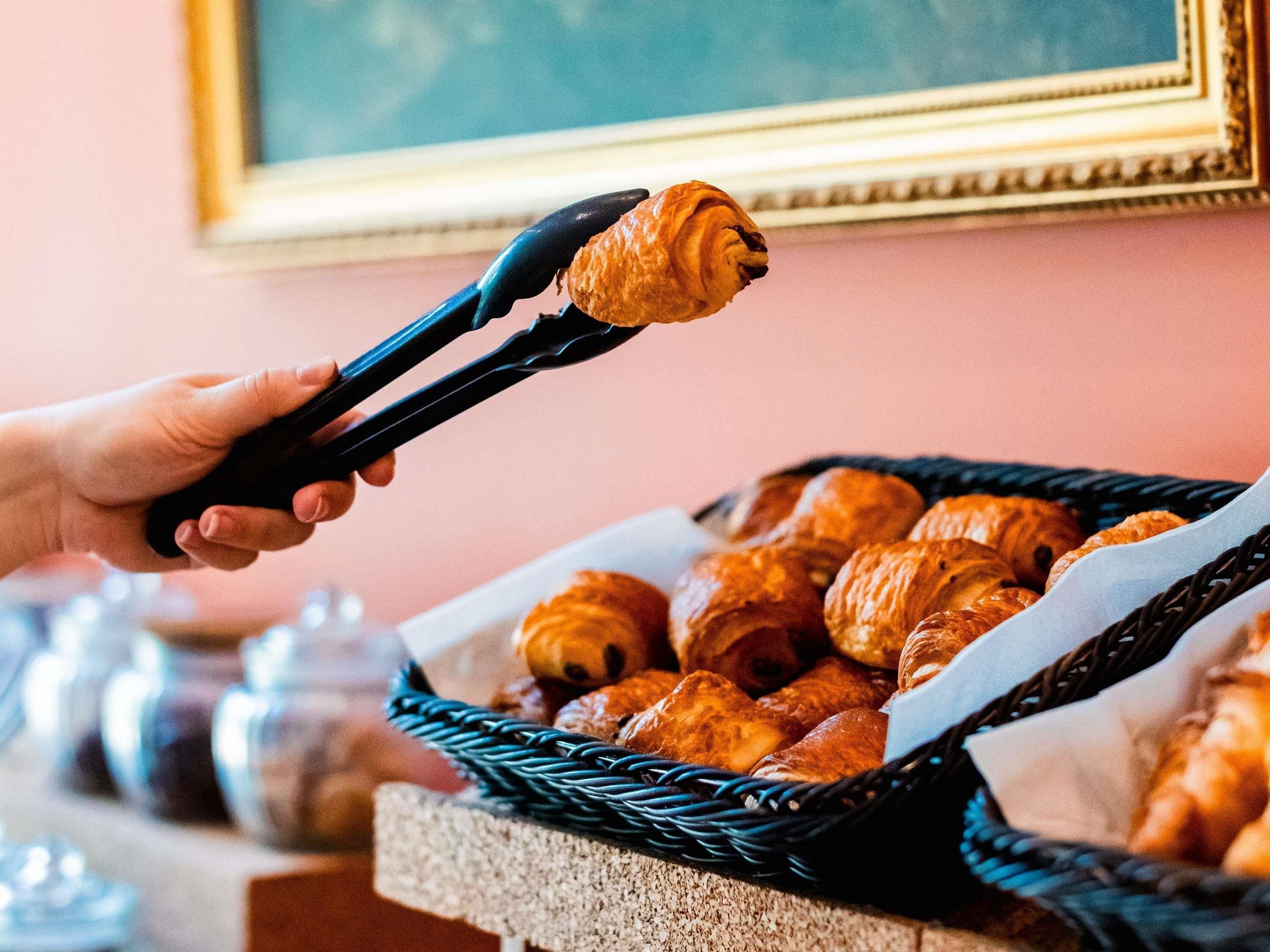 Een hand houdt tangen boven een mand croissants.