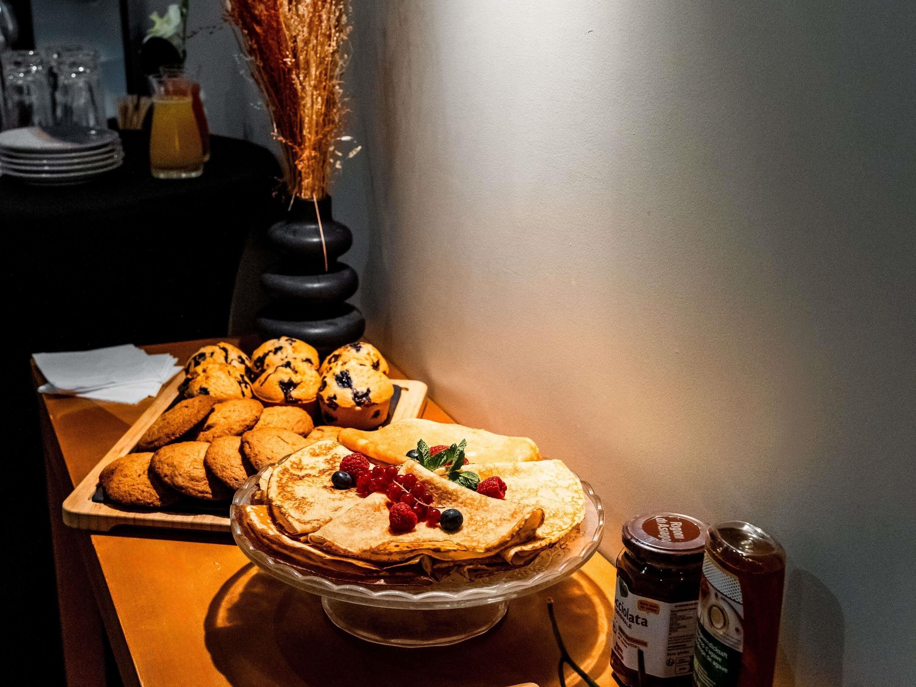A breakfast buffet with pancakes, muffins, and cookies on a wooden table.