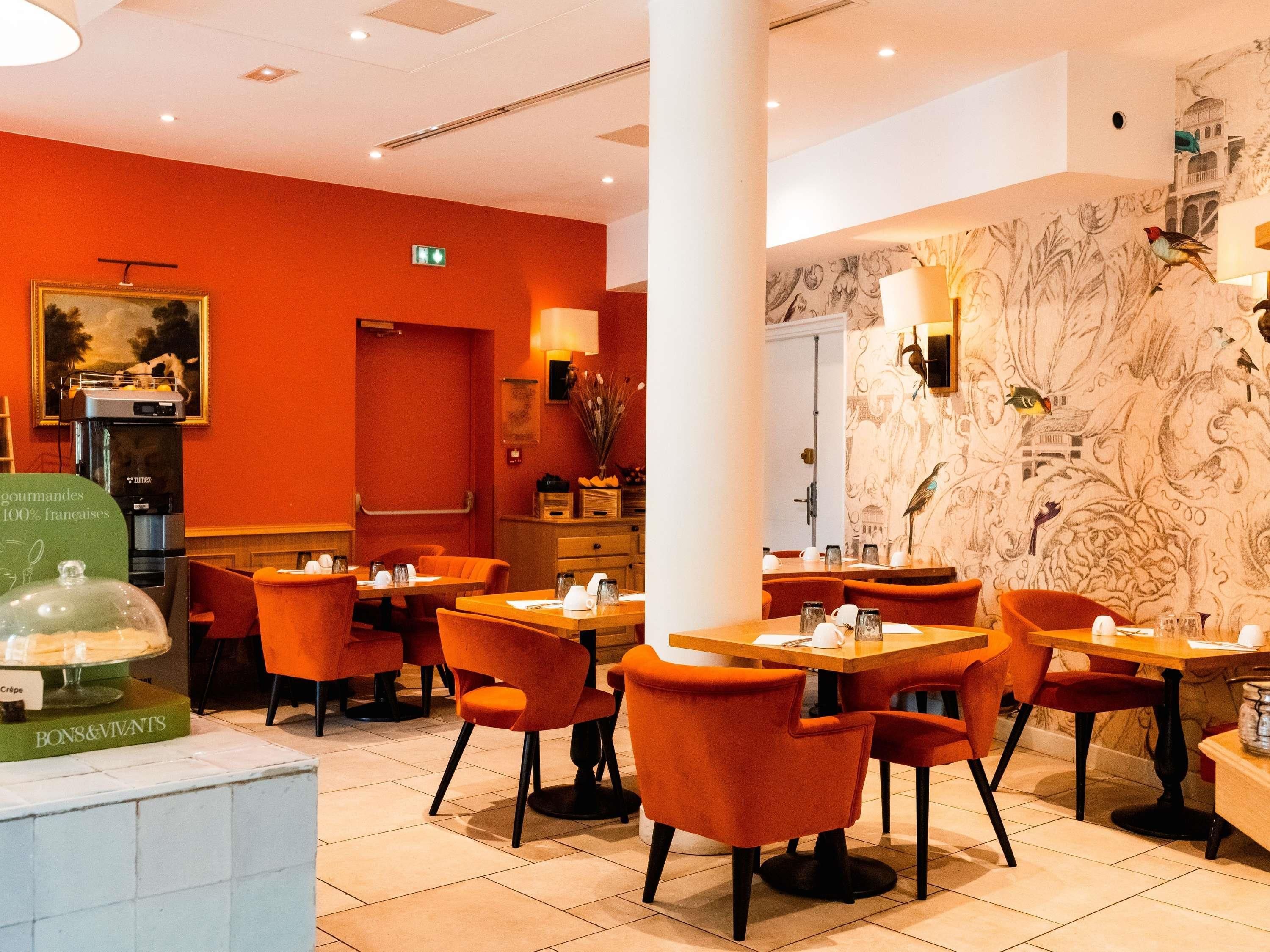 A restaurant interior with orange chairs, wooden tables, and a mural on the wall.