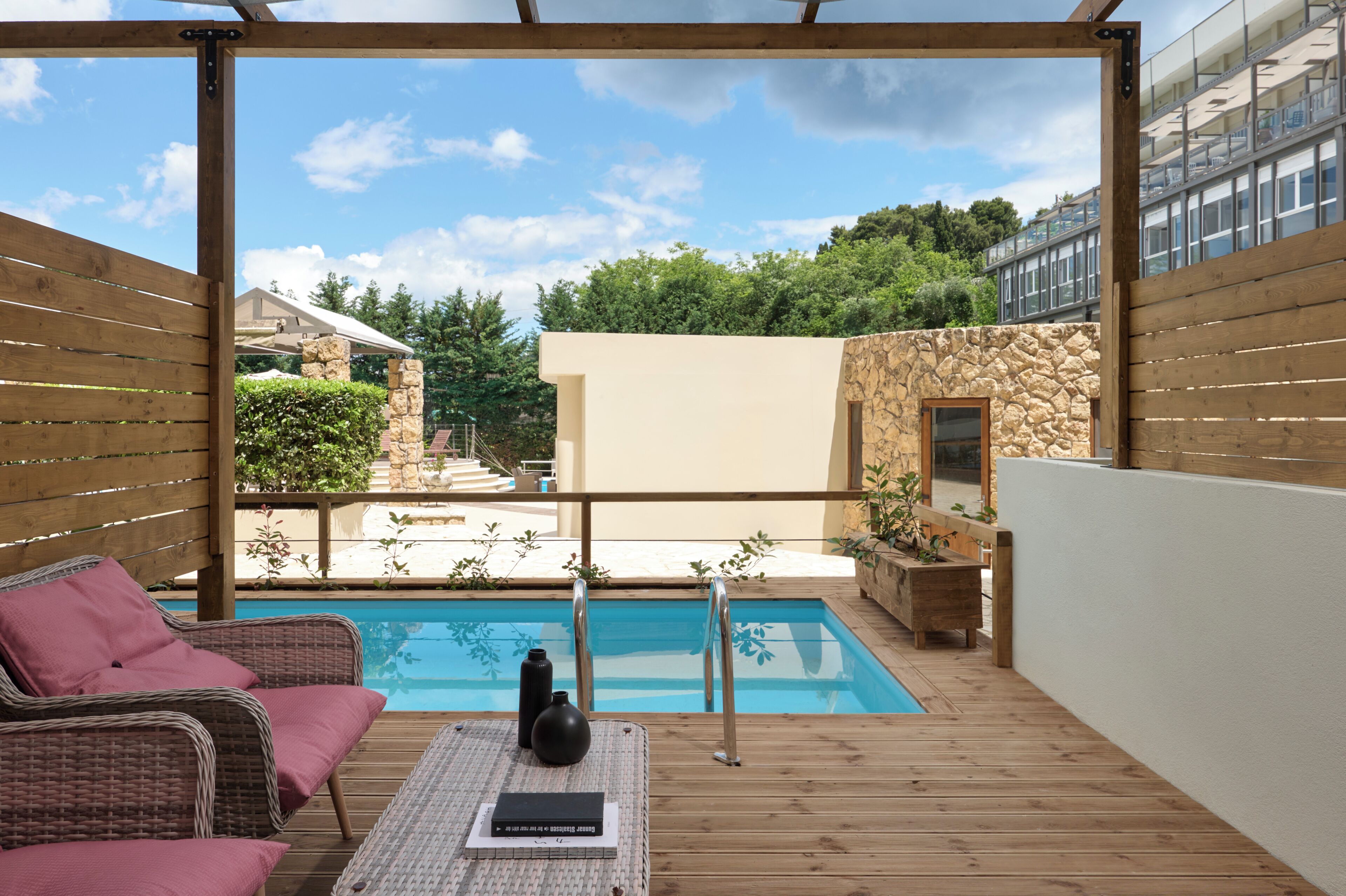 A wooden deck with a pool, wicker furniture, and a stone wall.