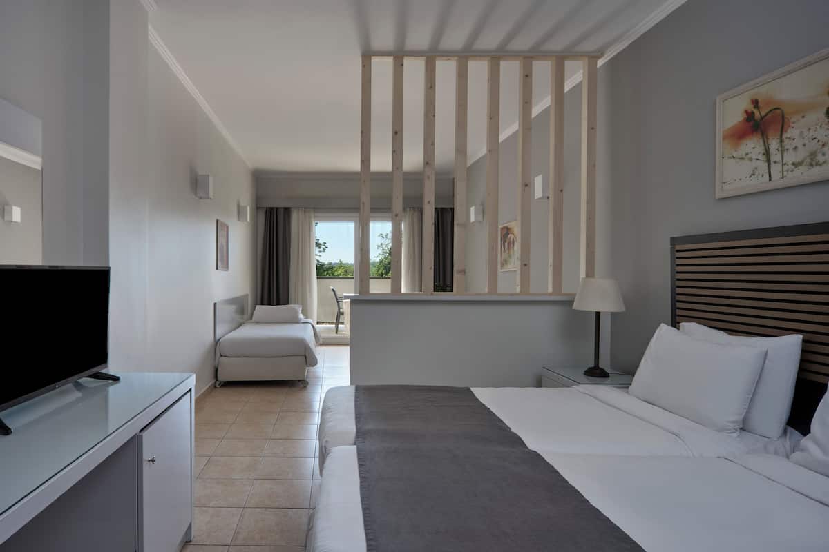 A hotel room with a bed, a TV, a desk, a chair, and a view of the outdoors.