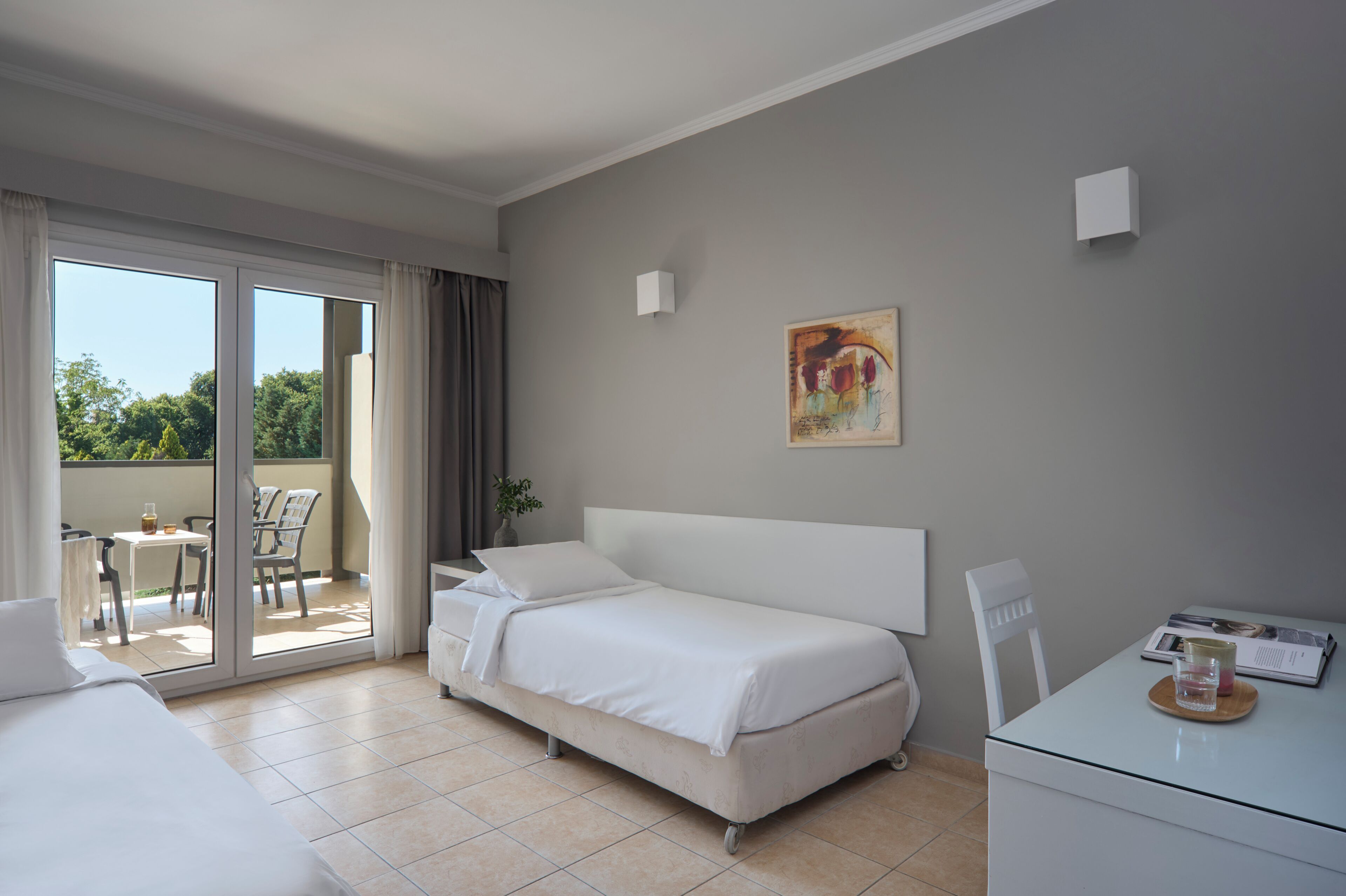 Een hotelkamer met een bed, een bureau, een stoel, een schilderij aan de muur en een schuifdeur naar een buitenruimte.