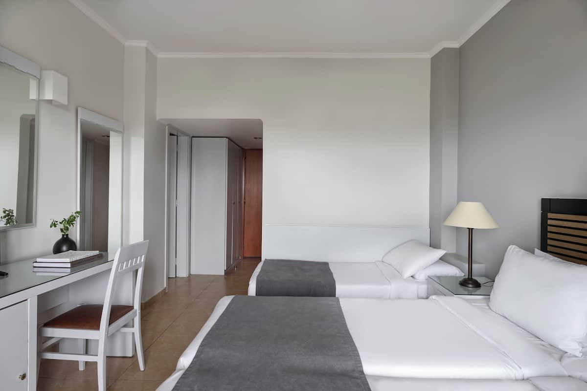 A hotel room with a desk, two beds, a lamp, and a mirror.