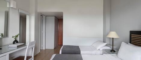 A hotel room with a desk, two beds, a lamp, and a mirror.