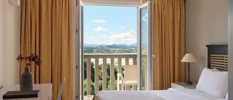 Ein Hotelzimmer mit Bett, Schreibtisch, Stuhl, Lampe und Blick ins Freie.