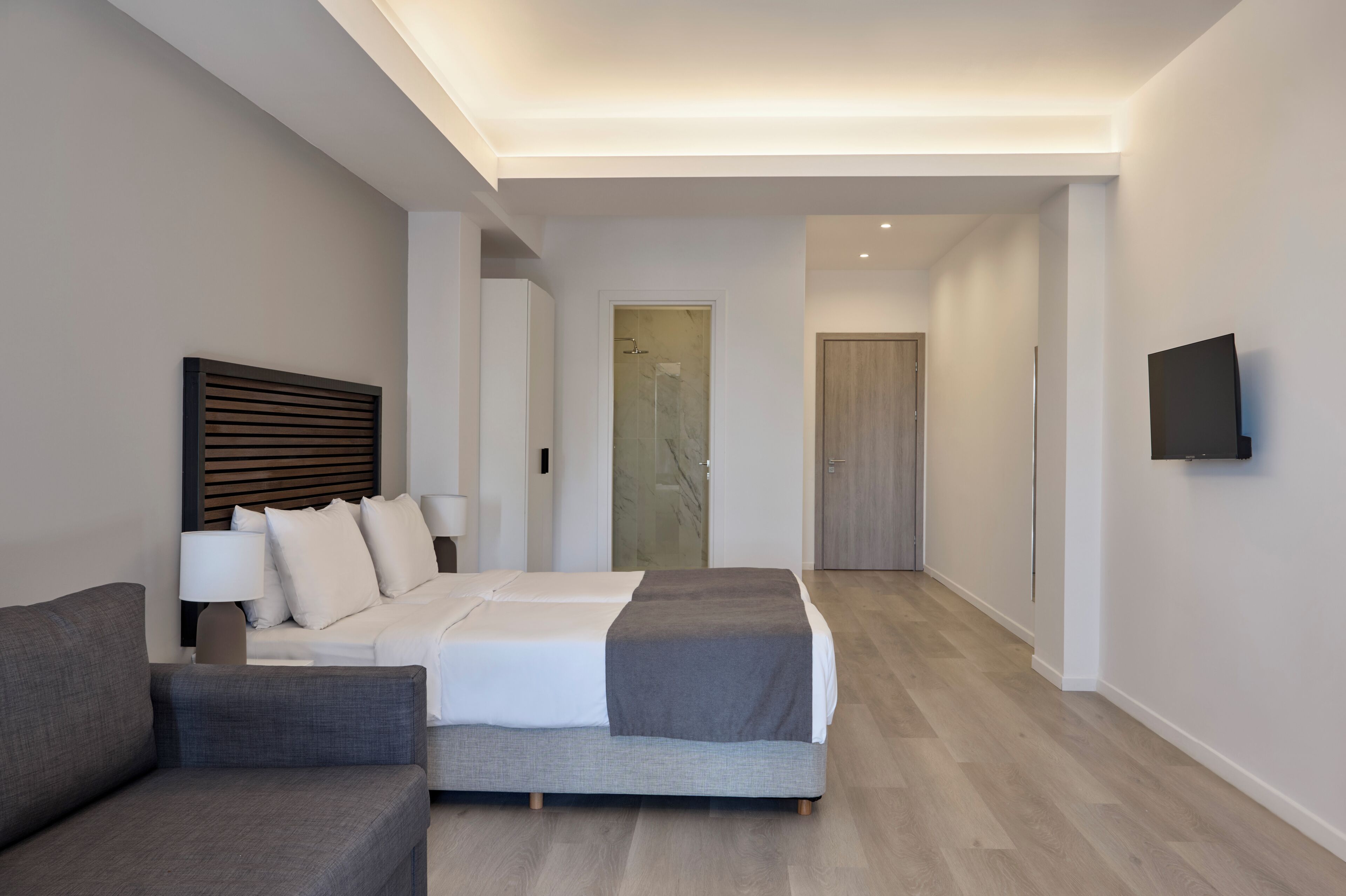 A modern hotel room with a bed, a sofa, a TV, and a walk-in closet.
