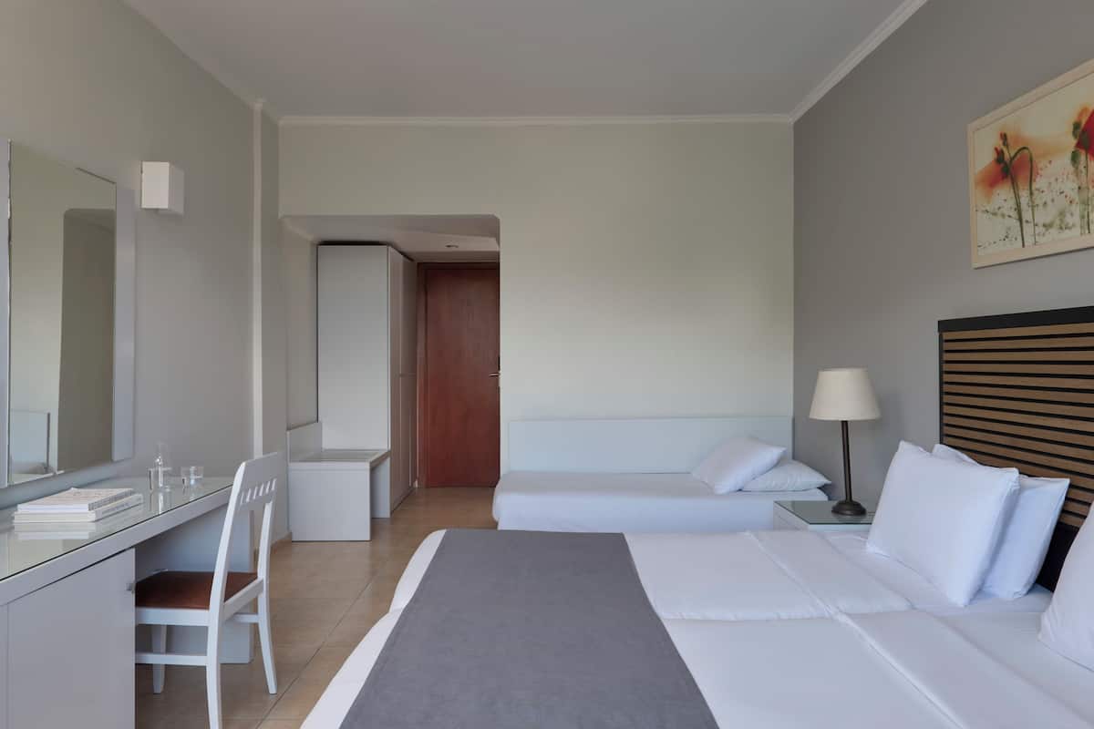 A hotel room with a bed, a desk, a chair, a bedside table, a lamp, and a painting on the wall.