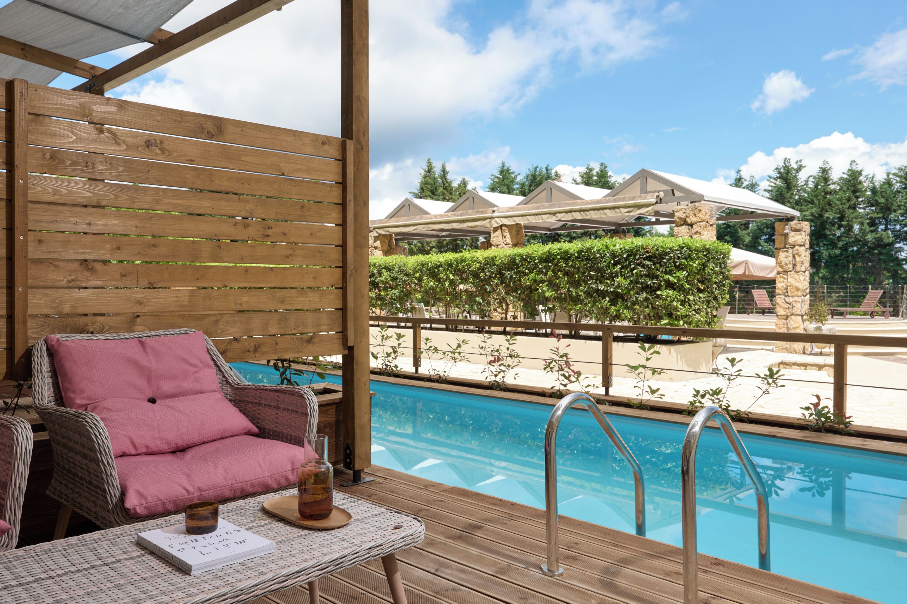 Eine Holzterrasse mit Pool, einem Korbstuhl und einem Tisch mit Getränk und Speisekarte.
