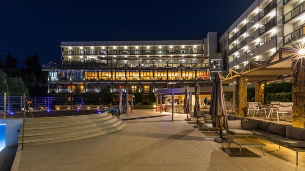 A modern hotel with a pool area, outdoor seating, and a well-lit facade at night. - Ariti Grand Hotel Corfu (Corfu)