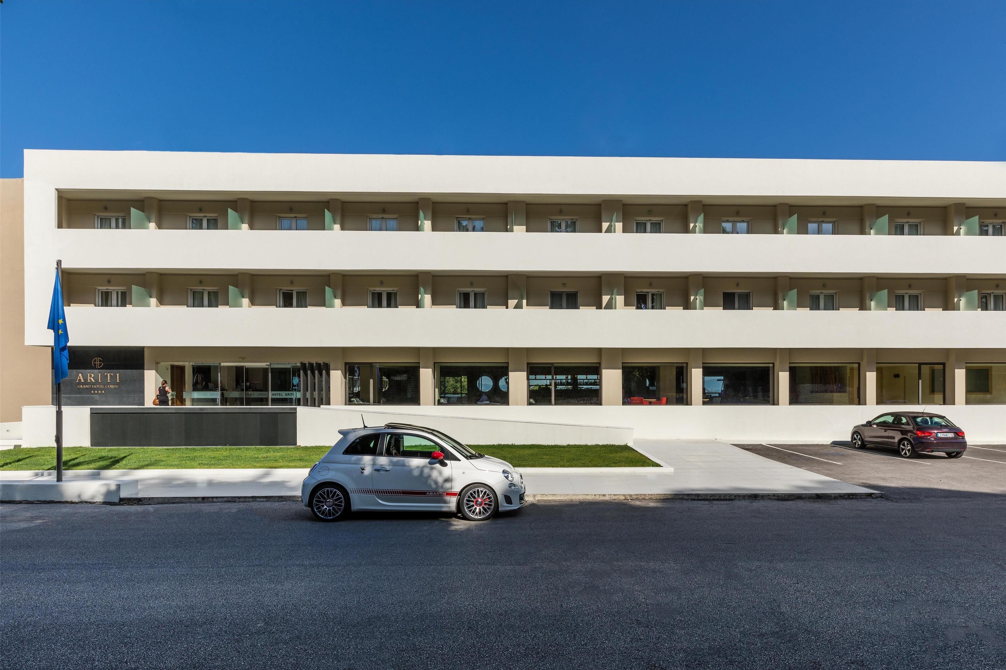 Un bâtiment moderne à la façade plate, doté de nombreuses fenêtres et d’un parking où sont garées deux voitures.