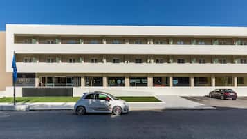 Un edificio moderno con fachada plana, varias ventanas y un estacionamiento con dos automóviles.