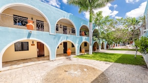 A courtyard with a fountain, a palm tree, and a building with multiple balconies and arches. - Hotel Hacienda Inn Aeropuerto (Mérida)