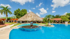 A swimming pool with a thatched-roof structure, palm trees, and a clear blue sky. - Hotel Hacienda Inn Aeropuerto (Mérida)