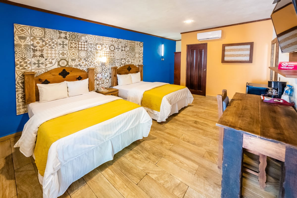 A hotel room with two beds, a wooden table, and a patterned wall.