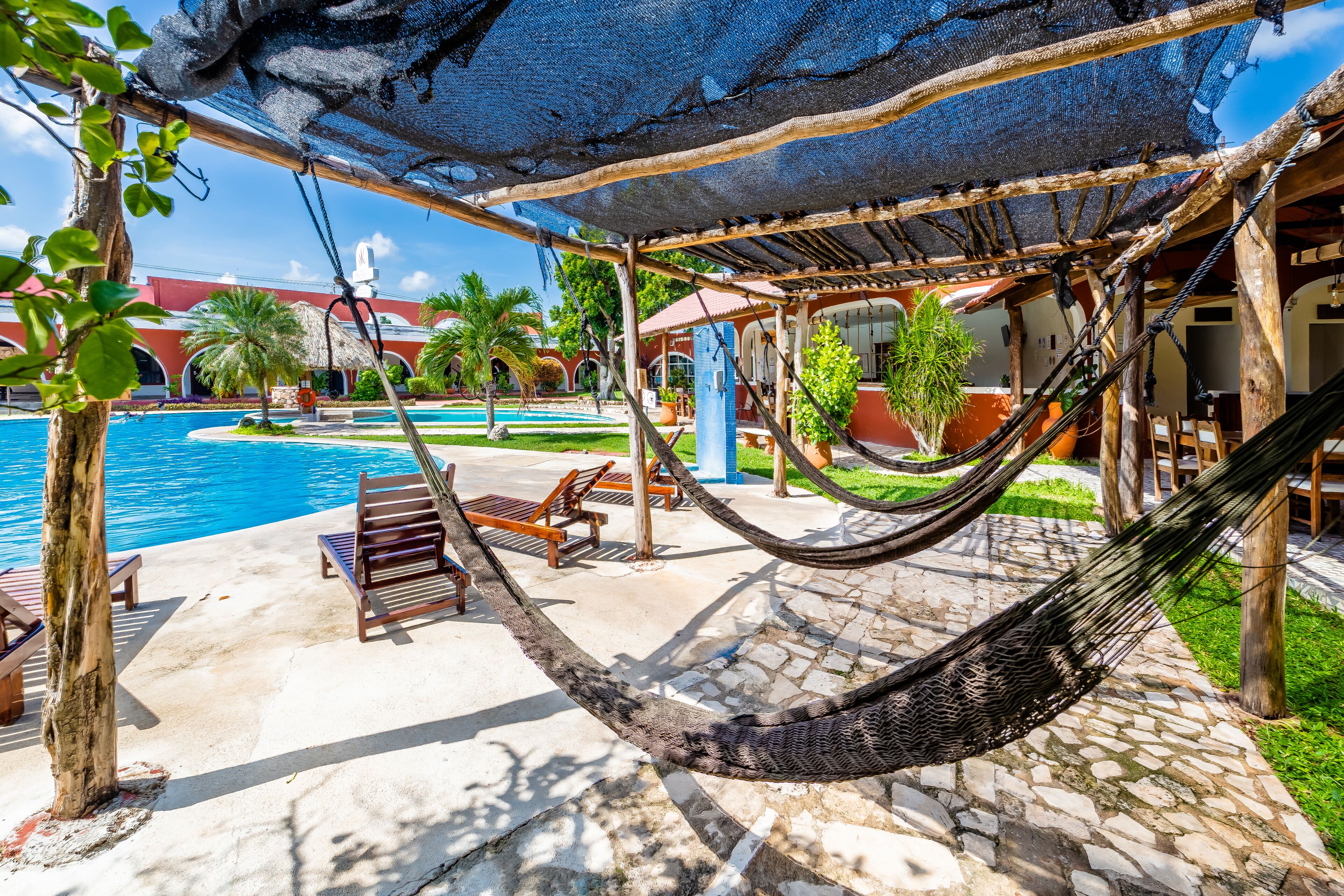Una hamaca bajo una zona sombreada, una piscina y sillas de descanso.