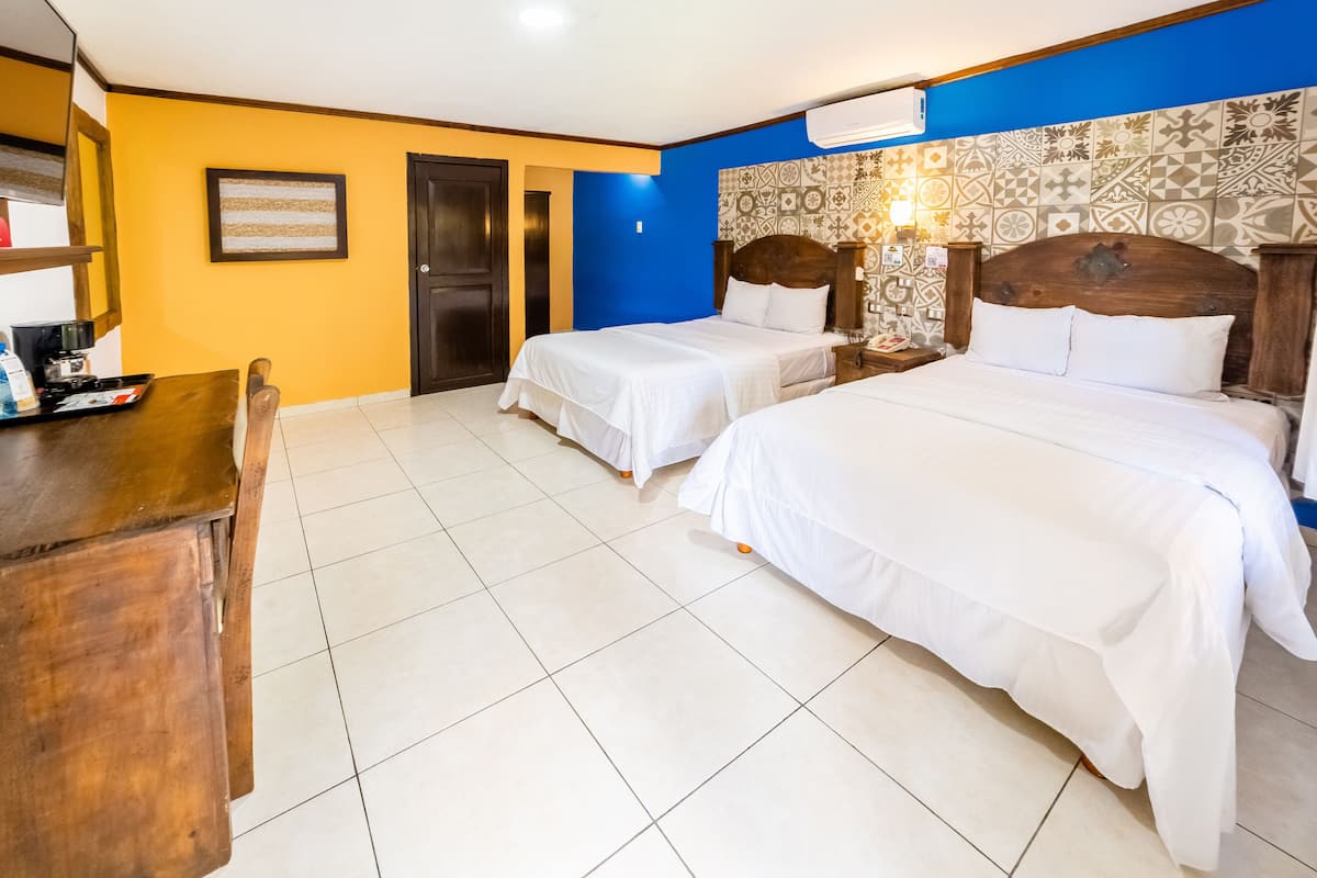 A hotel room with two beds, a wooden desk, and a tiled floor.