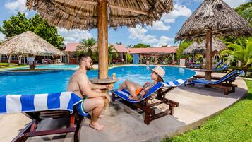 A poolside area with lounge chairs, a thatched umbrella, and a clear blue pool.