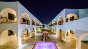 A nighttime corridor with arched balconies, a central water feature, and potted plants. - Hotel Hacienda Inn Aeropuerto (Mérida)