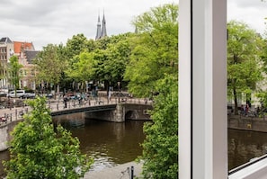 A canal with a stone bridge, surrounded by trees and buildings, including a church with two spires. - Max Brown Hotel Canal District, part of Sircle Collection (Amsterdam)