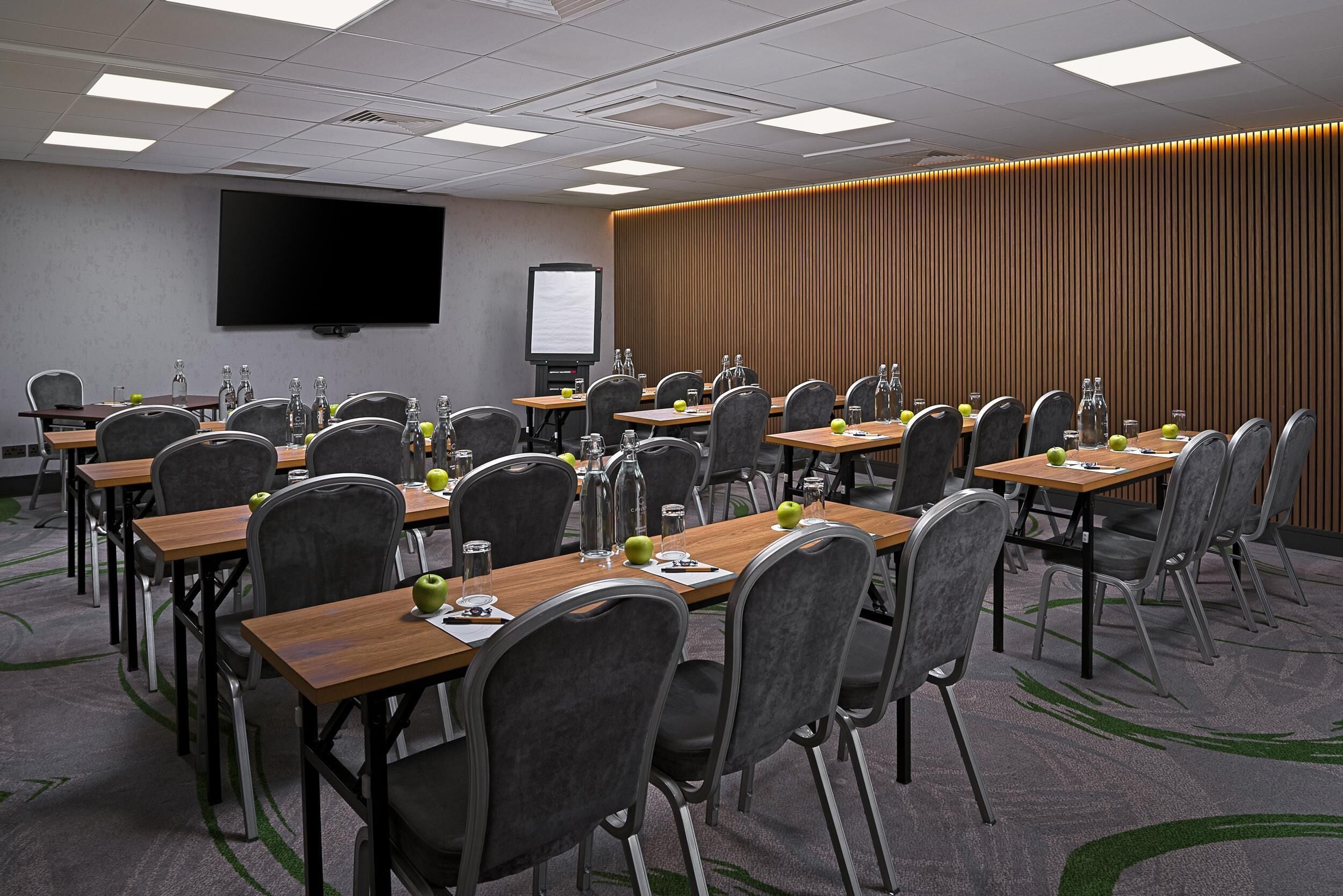 A conference room with multiple tables, chairs, a projector screen, and a whiteboard.