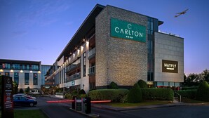 Un hotel con un llamativo letrero que dice 'Carlton', un restaurante 'Mayfly' y un diseño arquitectónico moderno.