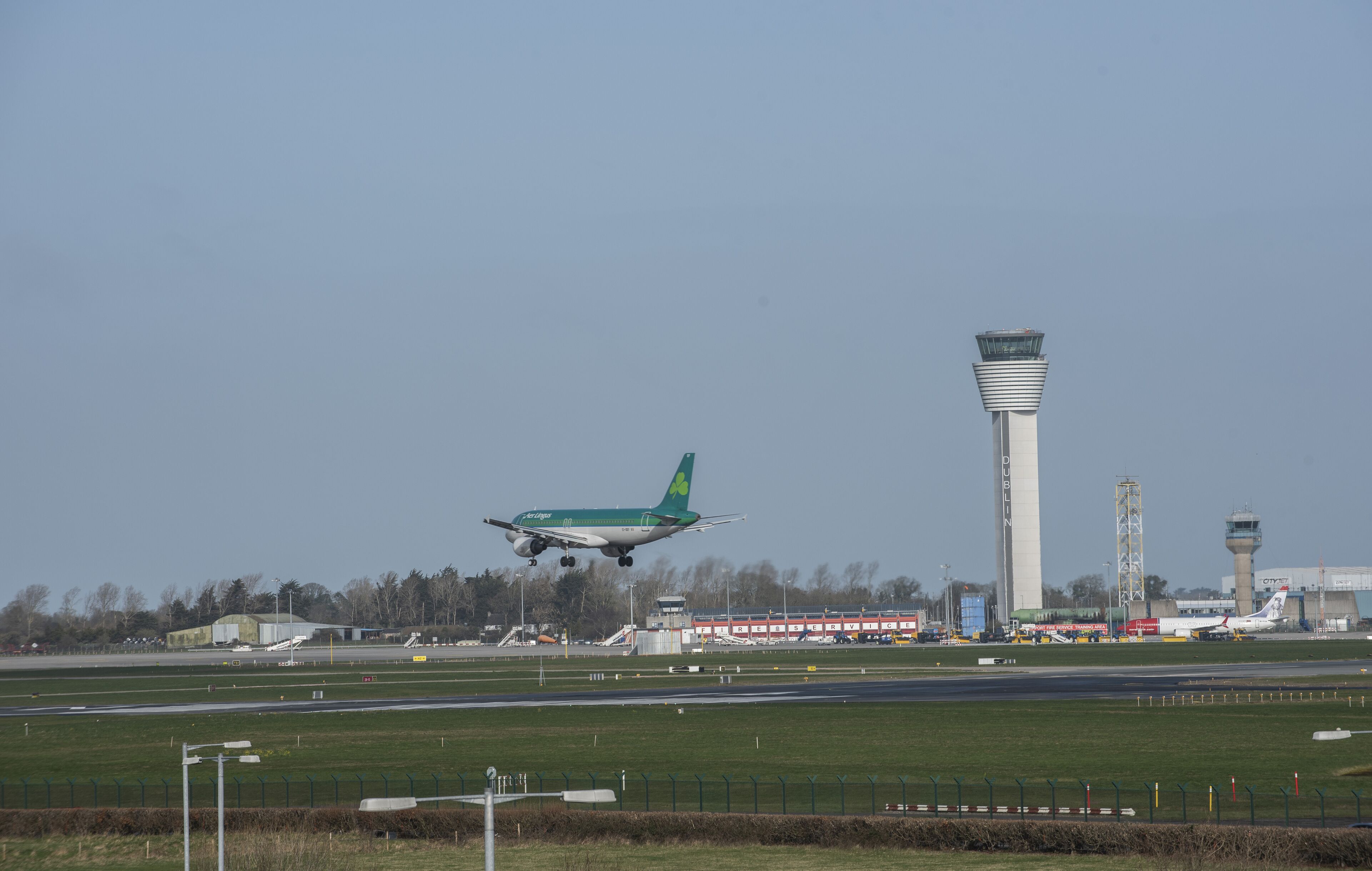 Un avión despegando de una pista, con edificios del aeropuerto y una torre de control al fondo.
