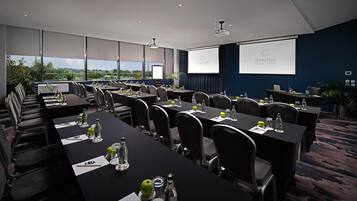 Un salón de conferencias con mesas, sillas, una pantalla de proyector y vistas de la ciudad.