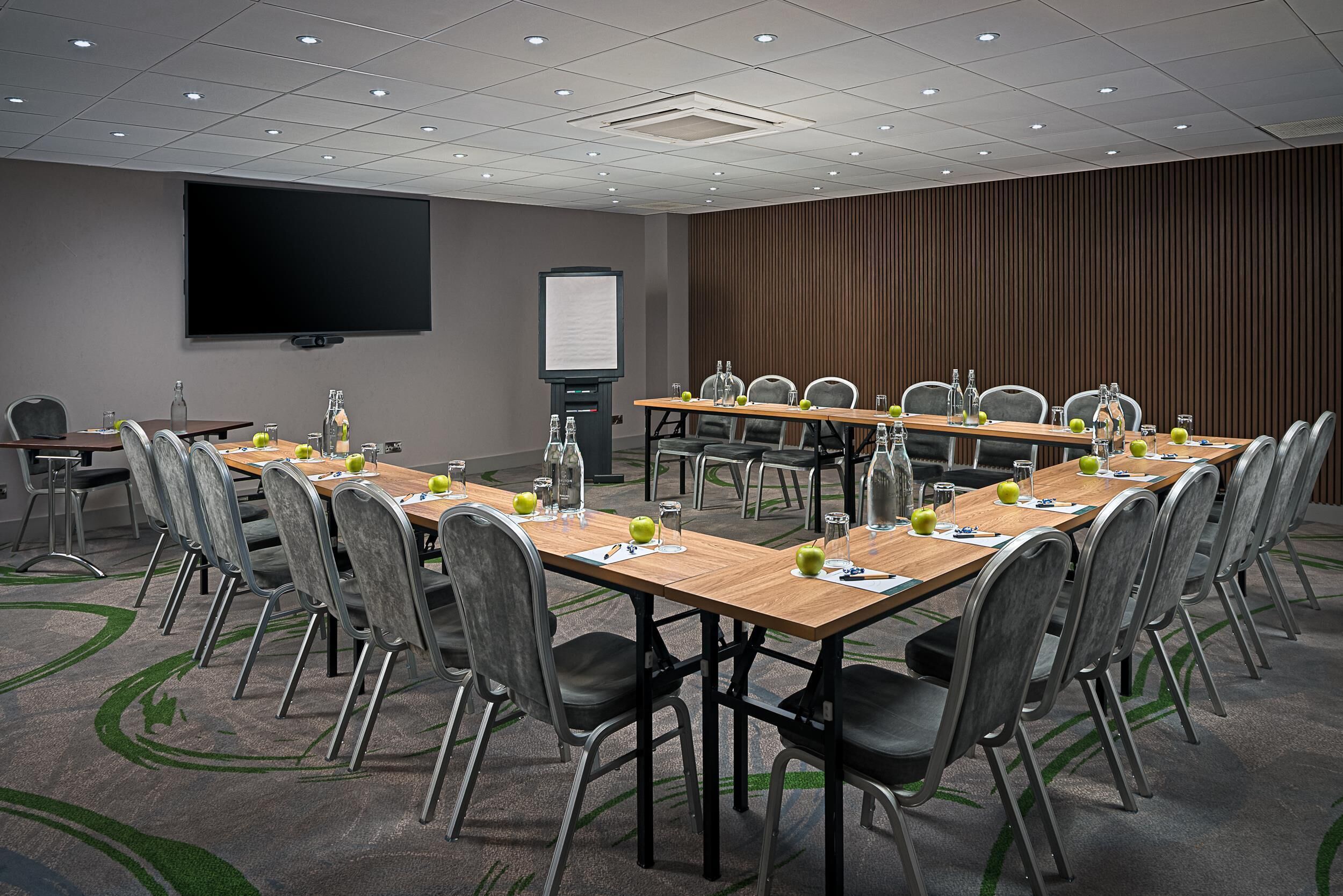 A conference room with a large flat-screen TV, a whiteboard, and a long table with chairs and water bottles.