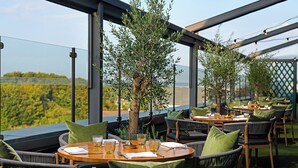 Un espacio de comedor al aire libre con mesas redondas, sillas de mimbre y cojines verdes.