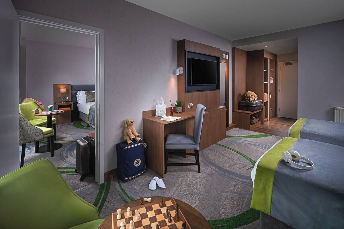 A hotel room with a desk, chair, TV, bed, and a small chess table.