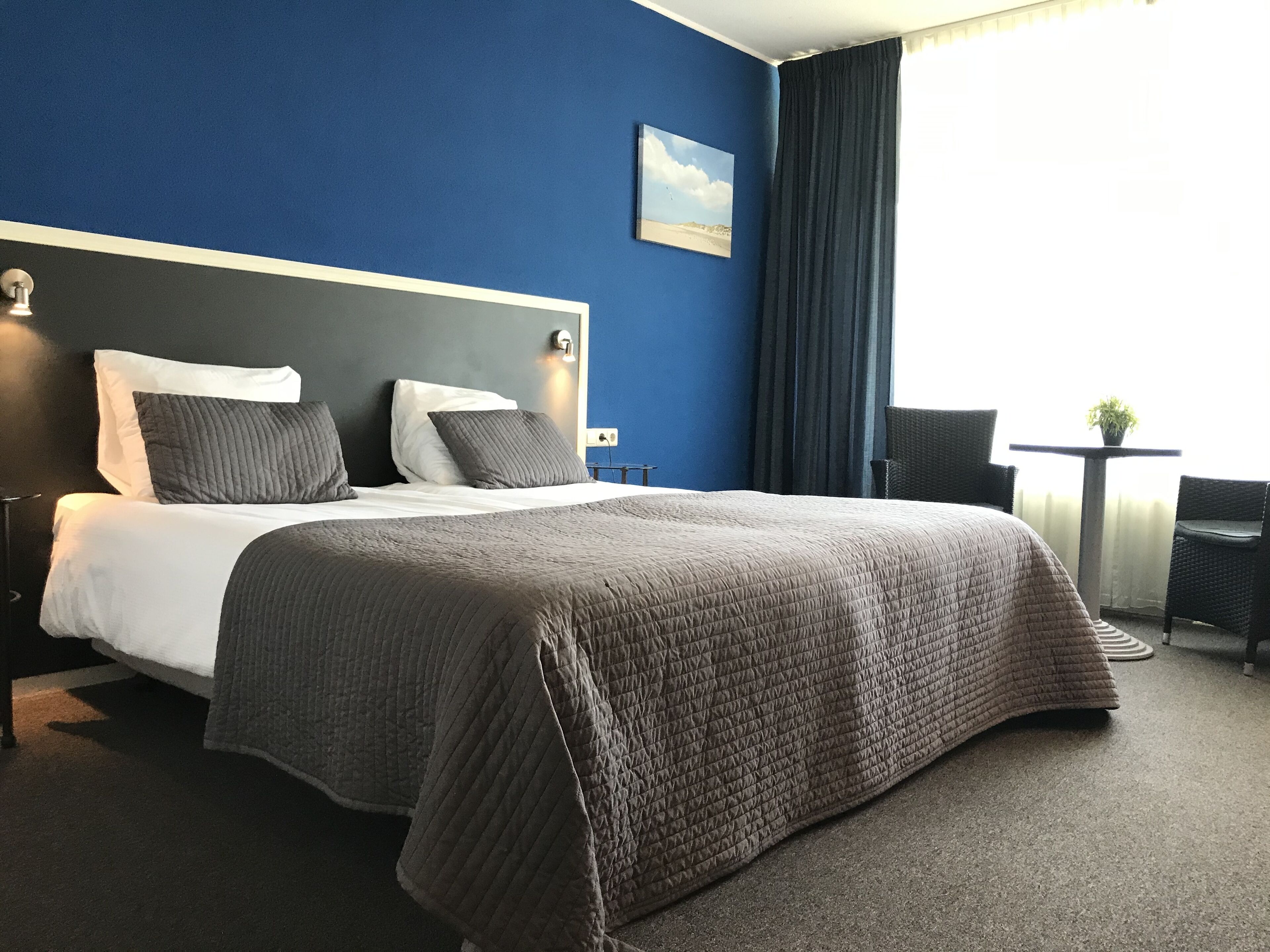 Een hotelkamer met een groot bed, een klein tafeltje met een plant en uitzicht op de omgeving.