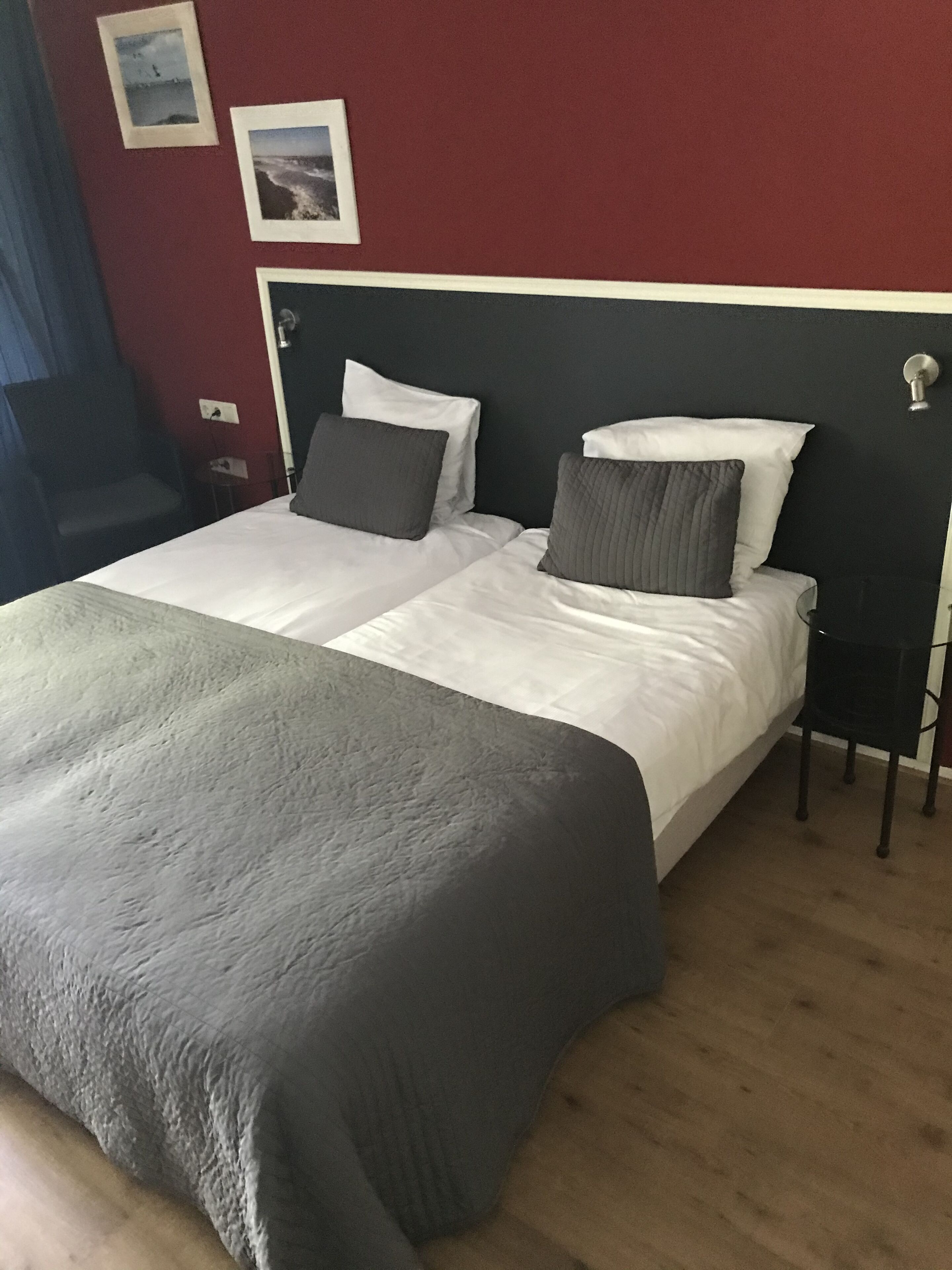 A double bed with a grey and white duvet, a black headboard, and a small bedside table with a lamp.