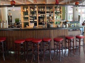 A bar area with multiple stools, shelves stocked with bottles, and a counter with various bar tools.