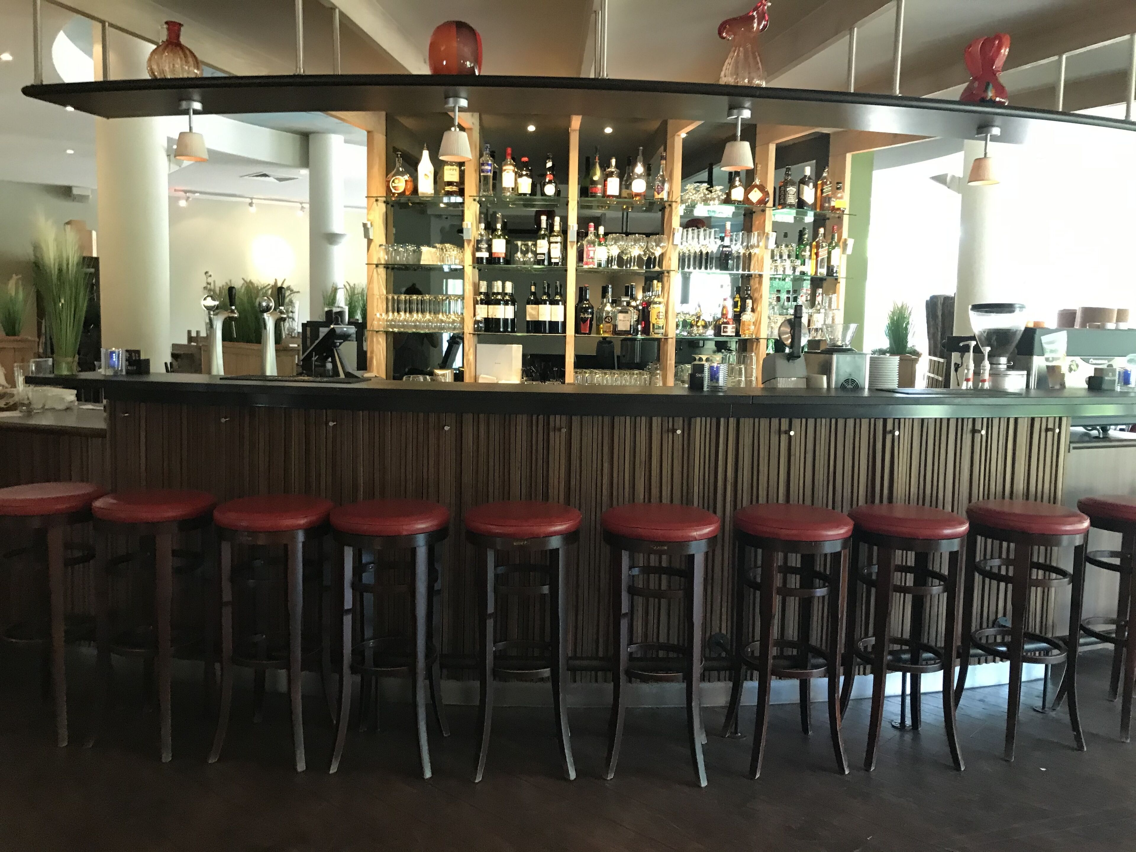 Una zona de bar con taburetes, estantes llenos de botellas y una barra.