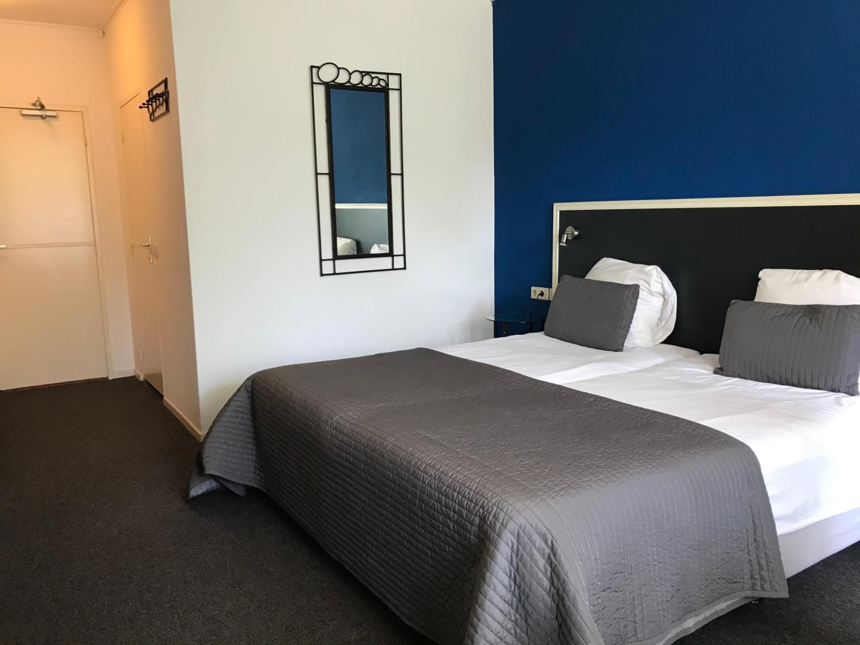 A bedroom with a bed, a nightstand, a mirror, and a door.