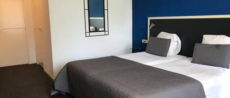 A bedroom with a bed, a nightstand, a mirror, and a door.