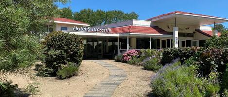A hotel with a covered entrance, a gravel pathway leading to the entrance, and various plants and shrubs around the property.