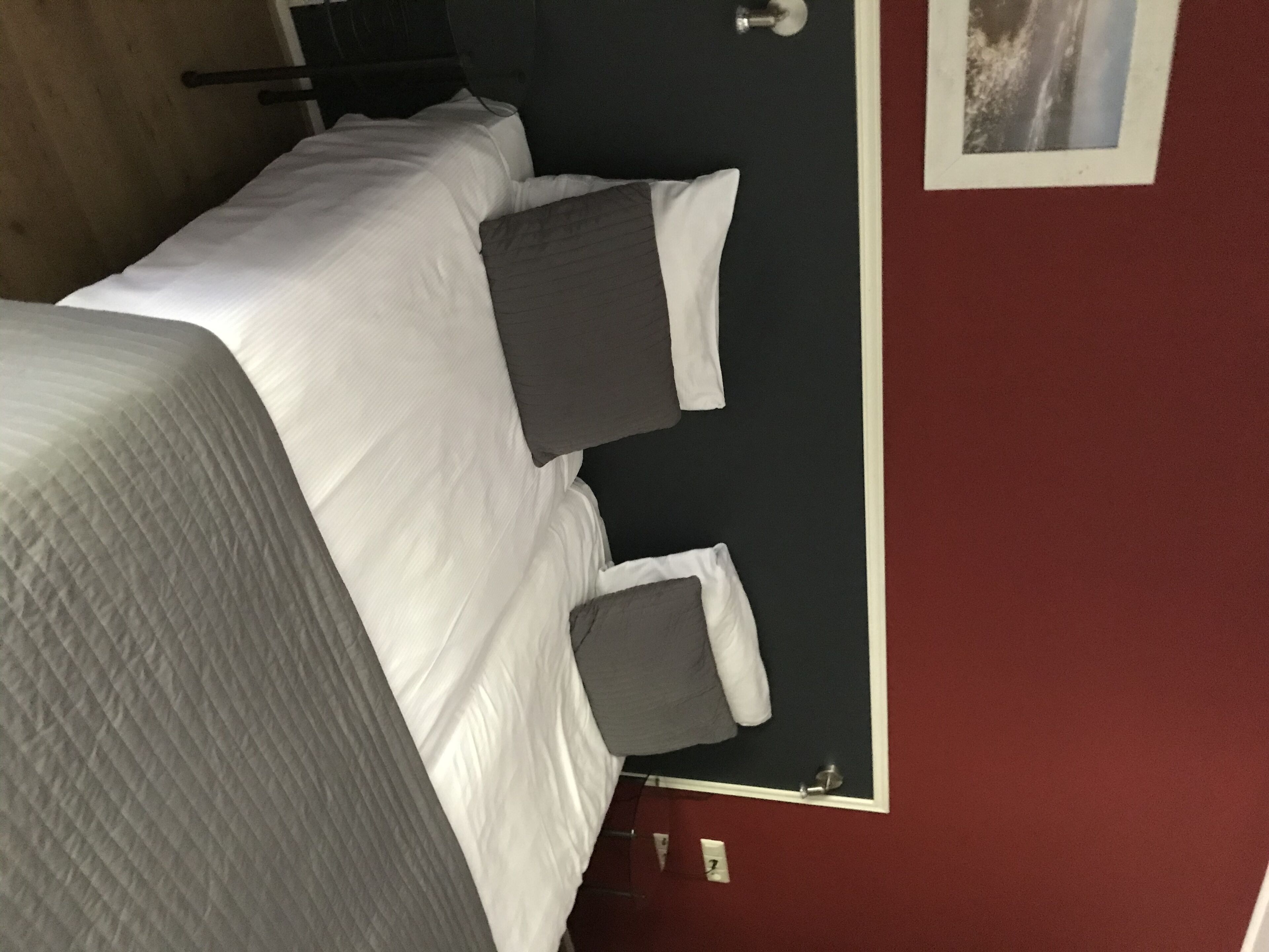 Ein Zimmer mit einem Bett, zwei Kissen, einer Tür und einem an der Wand hängenden Bild.